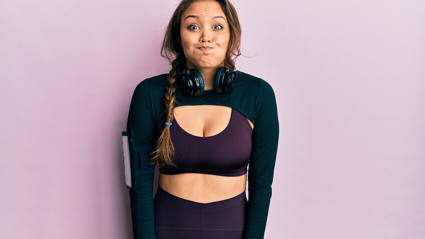 Young hispanic girl wearing sportswear and headphones puffing ch